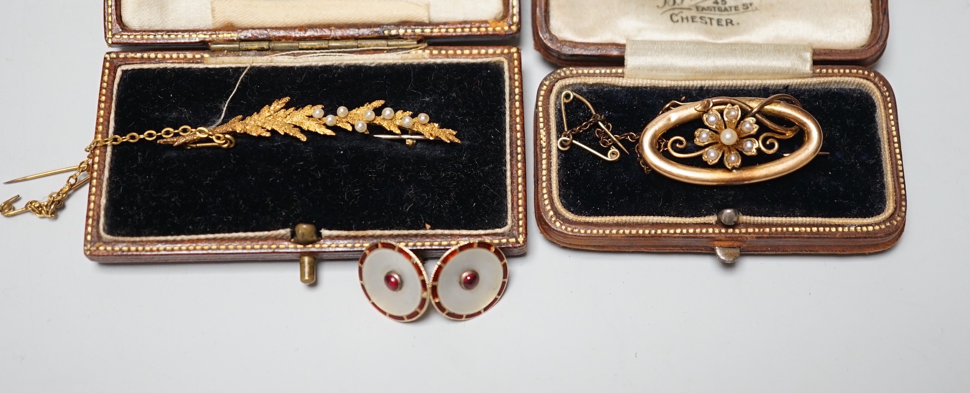 An early 20th century 15ct and seed pearl set leaf brooch, 51mm, one other 15ct and seed pearl brooch and a pair of 15ct, enamelled and gem set ear studs (converted buttons), gross weight 10 grams.
